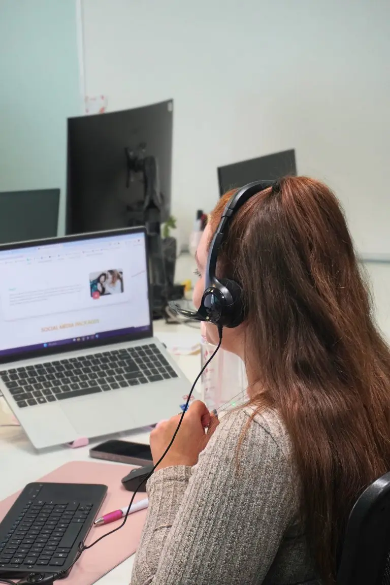 Woman wearing a headset working on a laptop with social media packages on screen.