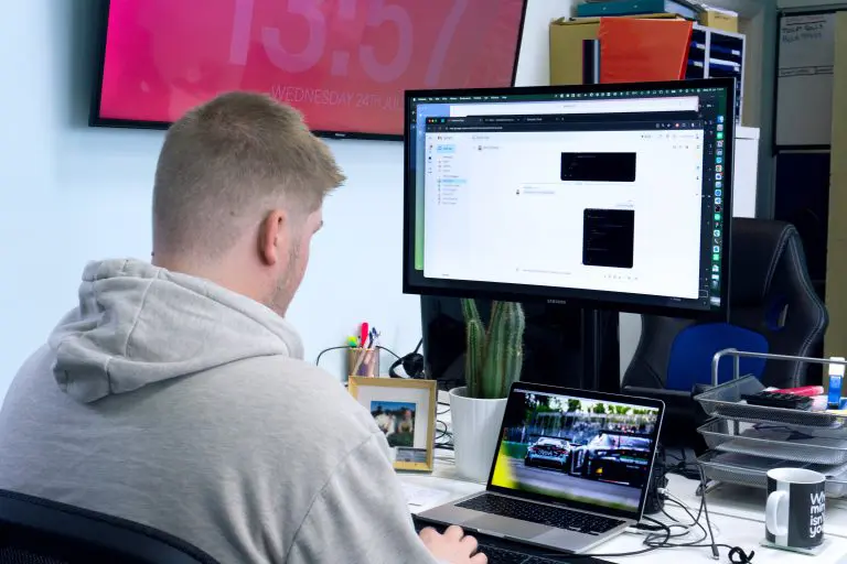 Person working on web development at a desk with a dual monitor setup in a digital agency office