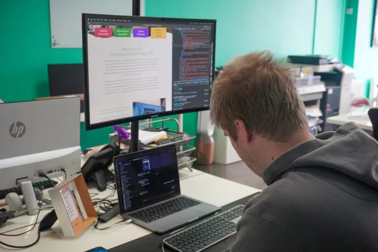 Web developer working on website code at dual monitor desk in office