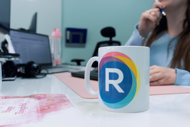 Resknow branded mug on office desk with team member working in background